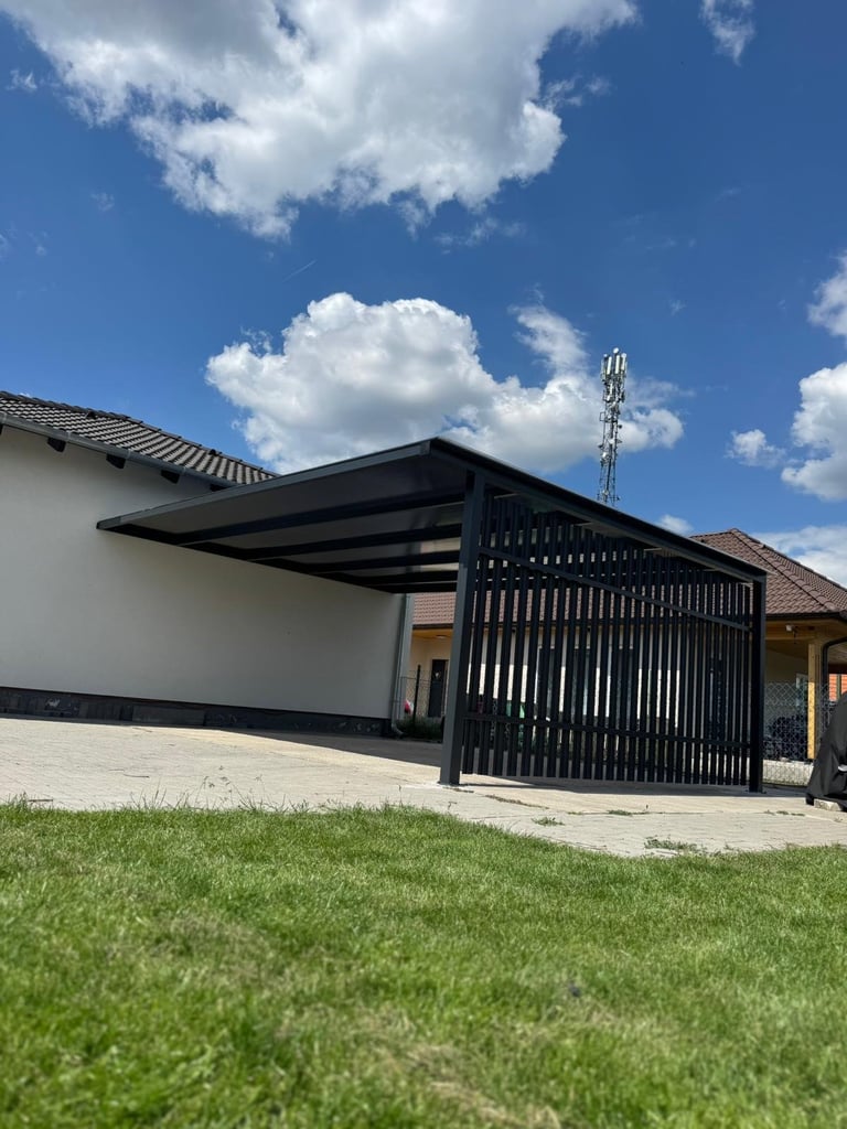Modern house with black metal carport and gate, white exterior wall, green lawn, and blue sky with white clouds