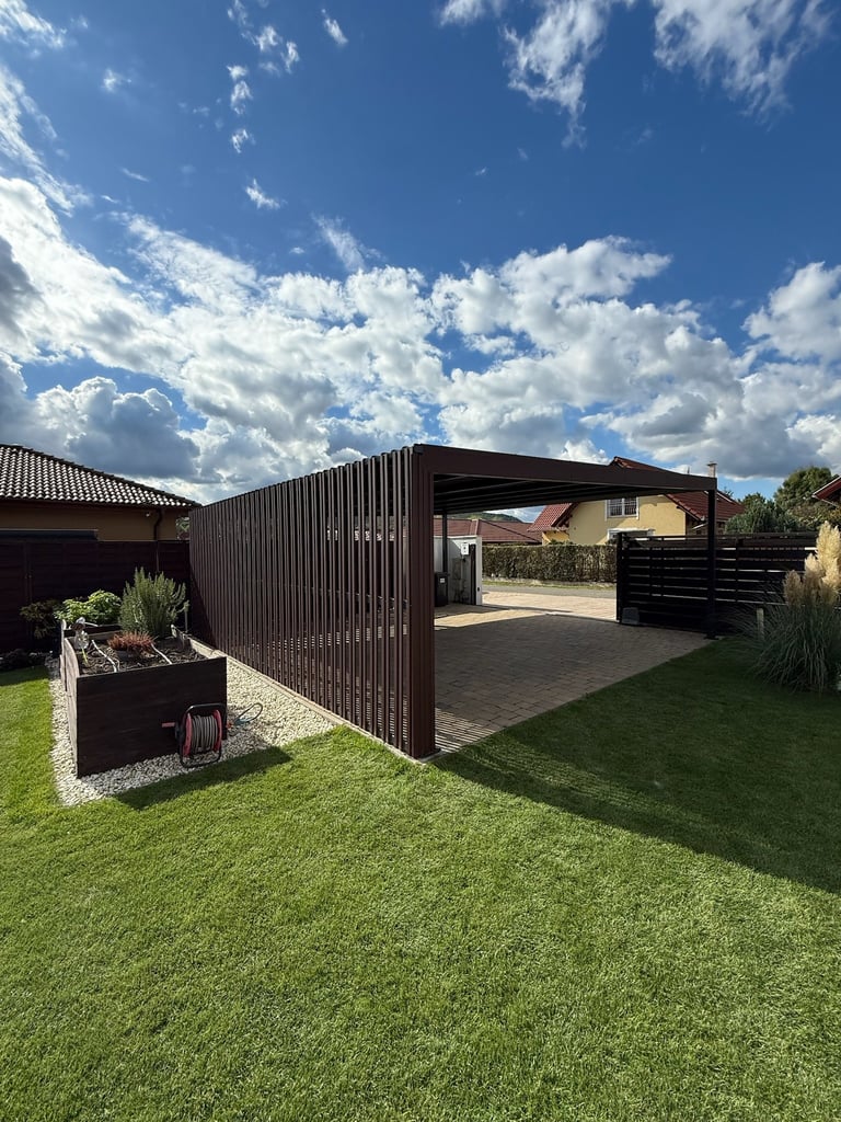 Modern black metal pergola and patio area in a manicured backyard with lawn and decorative planters under a blue sky